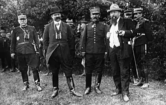 Photographie noir et blanc de 4 hommes debout, deux en uniforme et deux en civil.