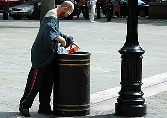 Homme fouillant une poubelle à Londres pour y trouver de la nourriture.