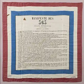 Texte imprimé en noir sur fond blanc sur un tissu carré aux bords bleu blanc rouge.
