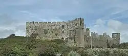 Photo d'un grand bâtiment de pierre grise dont les murs crénelés se découpent sur le ciel