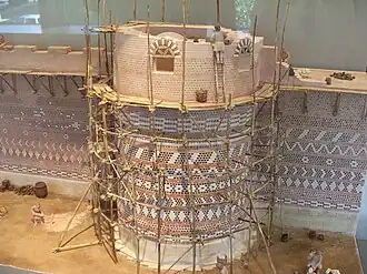 Maquette représentant une tour en construction avec des échafaudages en bois et des personnages