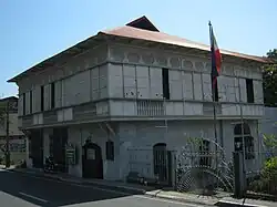 Une maison à étage. Une véranda ceint le premier étage, des panneaux coulissant permettant d'y accéder.
