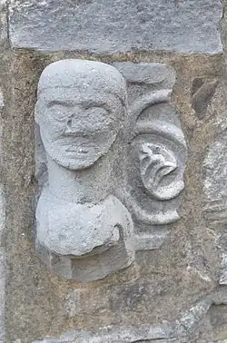 Fichée dans le mur extérieur du bas-côté sud, cette tête sculptée provient des fonts baptismaux mosans du XIIIe&nbsp;siècle disparus.