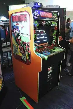 Photographie d'une borne d'arcade noire et orange, vue de trois-quarts droit, dans son ensemble.