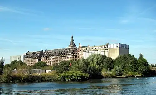 Bâtiment des Grands moulins à Marquette-lez-Lille de 1922 (béton armé et brique) de formulation historiciste, encadré par des ajouts de formulation de leur temps.