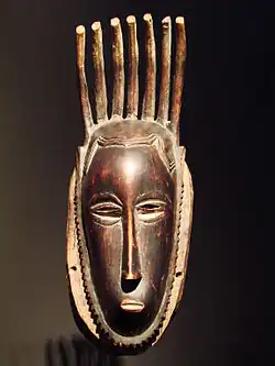 masque anthropomorphe en bois, allongé en hauteur, surmonté d'une coiffure sous forme de bâtons érigés verticalement