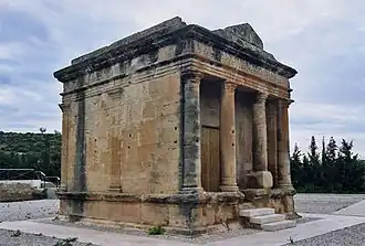 Photographie en couleurs d'un monument antique parallélépipédique.