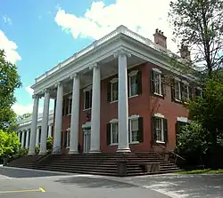 Un bâtiment en briques rouges avec des colonnes blanches supportant son avant-toit. Ce dernier donne sur une route.