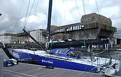 Vu de trois quarts arrière, voilier bleu et blanc amarré au ponton.