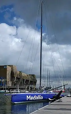 Vu en entier, de trois quarts avant, voilier bleu et blanc amarré au ponton.