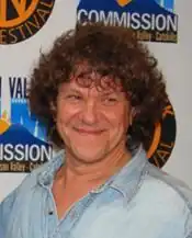 Photo d'un homme souriant, aux cheveux blonds bouclés, portant une chemise bleue.