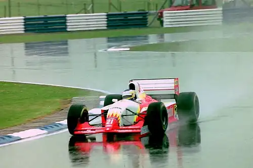 Photo d'une monoplace de Formule 1 de couleur rouge, jaune et blanche sur une piste détrempée