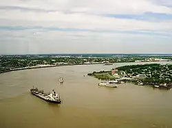 un large fleuve ocre, quelques gros bateaux. Sur les rives se déploie une ville verdoyante.