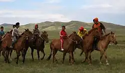 Plusieurs enfants montent des chevaux roux et marrons dans un paysage de steppes montagneuses.