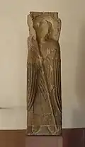 Dans le même bloc, sur la face antérieure de la stèle du XIIe&nbsp;siècle, l'évêque saint Léger (« S.Levdga » dit aussi Leodegar ou Leutgar) qui soutient la construction des bâtiments claustraux. On distingue la tête de l'évêque qui a été martelée au cours de la Révolution.