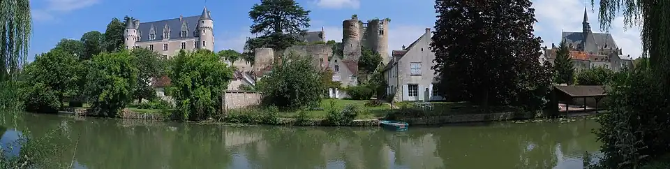 Photographie en couleurs d'un château Renaissance, de tours médiévales et d'une église du XVe&nbsp;siècle en arrière-plan d'un village au bord de l'eau.