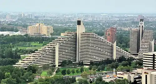 Une grande pyramide vue presque de face et une autre vue de profil au milieu du parc olympique. En fond, on voit le reste de la ville de Montréal.