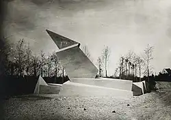 Photographie en noir et blanc d’un monument aux morts. Sculpture en béton aux formes anguleuses.