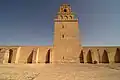 Gros plan sur la façade nord de l'édifice. Au milieu du mur, pourvu de contreforts à toit en pente, se dresse l'imposant minaret crénelé.