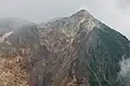 Photo couleur d'une montagne à la face avant érodée, sous un ciel nuageux.