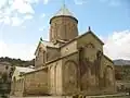 Monastère en forme de temple en croix avec arcatures en pierre de couleur sable et surplombé par un clocher surmonté d'une croix orthodoxe.