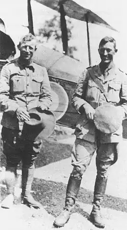 Photo en noir et blanc représentant deux hommes debouts, souriants en tenues militaires.