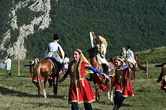 Groupe de cavaliers et de chanteurs, une chanteuse habillée en rouge et or au centre.
