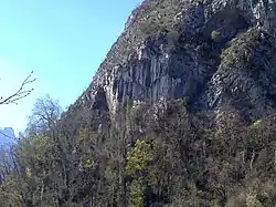 Parois rocheuses se terminant par une grotte, pratiquement envahie par la végétation.