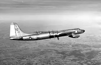 Photographie en noir et blanc d'un avion en vol, avec, en fond, la surface de la Terre.