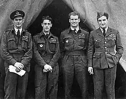 Photographie noir et blanc de quatre hommes, debout, de face, en uniforme de pilote.