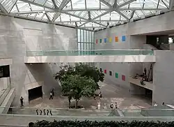 Grand hall à l'intérieur d'un bâtiment moderne et lumineux, avec un arbre et des passages empruntés par des piétons.