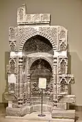 Mihrab en pierre décoré de motifs floraux et des versets 18 et 19 de la sourate al-Imran.