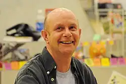 Portrait d'un homme chauve souriant prise dans une librairie.