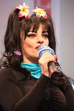 Image d'une femme brune avec des fleur dans les cheveux parlant dans un micro