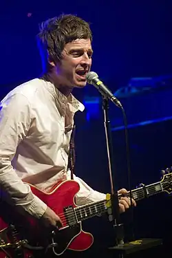 Photo d'un homme chantant dans un micro et jouant de la guitare.