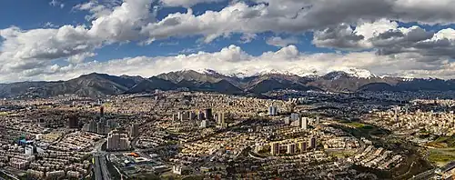 Devant de belles montagnes enneigées une grande ville, composée de quelques immeubles de grande hauteur, énormément de bâtiments, certains relativement bien rangés, d'autres s'accumulant sans ordre apparent, et quelques axes de circulation qui les traversent.