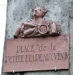 Plaque de rue en terre cuite rouge, avec personnage, raisins, bouteilles et tonneaux