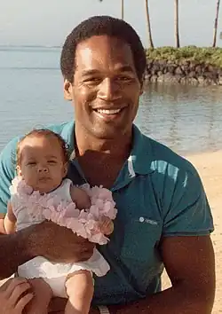 Un homme et une femme tenant un jeune enfant sur une plage paradisiaque.
