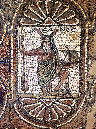 Représentation d'Océan, surmonté de son nom grec Ὠκεανός / Ōkeanós (écrit ωΚΕΑΝΟϹ), avec ses attributs habituels : pinces de crustacé sur la tête et rame à la main, auxquels ont été rajoutés ici un navire et un dauphin. Église byzantine de Pétra (Jordanie), aile sud, mosaïque (VIe siècle).