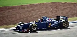 Photo d'une voiture bleue en piste. Au second plan, de l'herbe et de la terre.