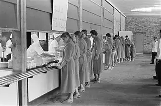 Une longue file de femmes en robe longue attendent d'être servies à une cantine.
