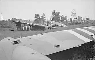 Photo en noir et blanc représentant des planeurs démantelés au sol, dans un champ, avec des arbres à l'arrière-plan.