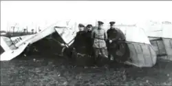 Photo noir et blanc de quatre hommes en uniforme posant à côté de la carcasse d'un avion au sol.