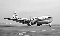 Vue de trois-quarts avant d'un avion de ligne à hélices ; la partie inférieure du fuselage est en métal nu, la partie supérieure est peinte en blanc et porte l'inscription « Pan American World Airways ».