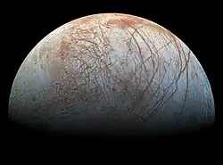 La moitié de la lune est dans la lumière. Des lignes et brunes contrastent avec la surface grisâtre.