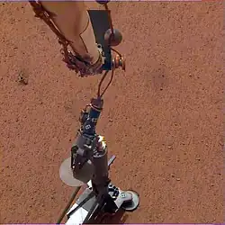 Photo montrant le bras robototique et l'instrument HP3 peu après la dépose de ce dernier sur le sol