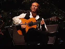 Photo d'un homme assis jouant de la guitare.
