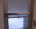 Barre anti-panique, poignée de secours installée sur une porte extérieure en verre.