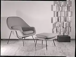 Photographie en noir et blanc d’un fauteuil et son repose-pieds sur un parquet.