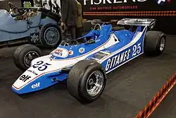 Photo de d'une monoplace blanche et bleue, sans aileron avant, à une exposition.